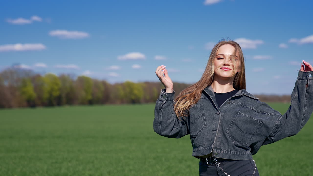 Happy girl on a meadow. Attractive young model with lovely face in denim suit posing on camera and smiles. Portrait of a young woman in nature in a sunny day.