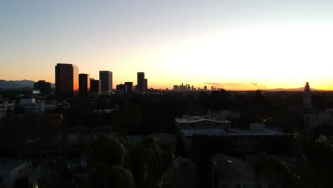 Palm-tree-silhouette-reveals-beautiful-Los-Angeles-downtown-buildings-in-the-horizon-on-an-early-morning-sunrise