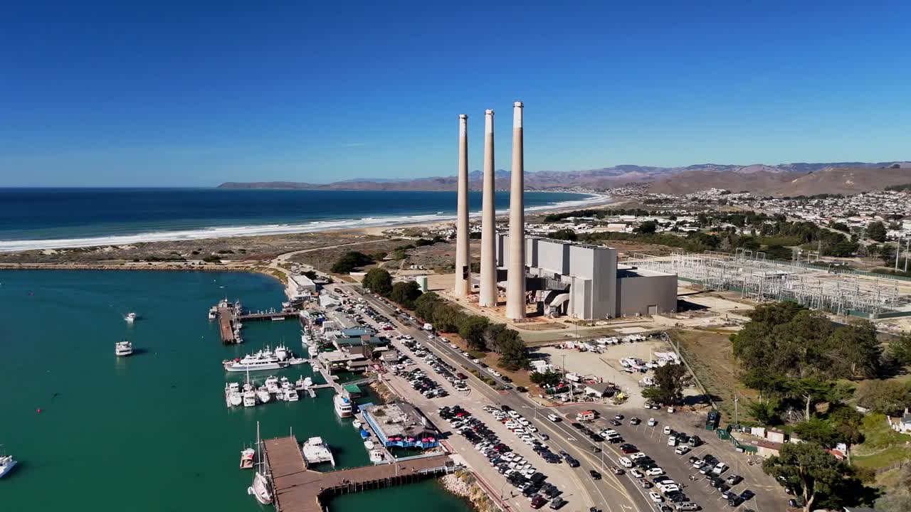 A wide aerial shot capturing the harbor, boats, and calm coastal waters of Morro Bay on a clear California day