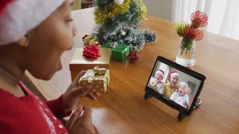 Afroamerikanische-Frau-Mit-Weihnachtsmütze-Nutzt-Tablet-Für-Weihnachtsvideoanruf-Mit-Der-Familie-Auf-Dem-Bildschirm