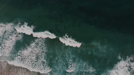 Birds-eye-view-of-beautiful-clear-blue-waves,-rising-drone-shot