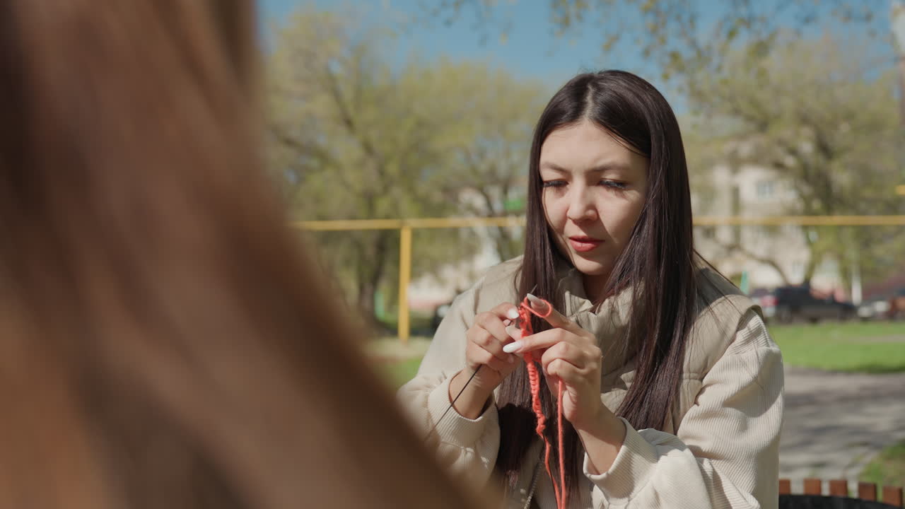 화창한 공원 행사에서 뜨개질 교육을 위해 야외 커뮤니티가 모였어요. 멘토는 햇볕이 잘 드는 공원 행사에서 참가자들에게 뜨개질을 지도하고, 아시아인 강사는 평화로운 공원 환경에서 뜨개질 워크숍을 진행합니다.