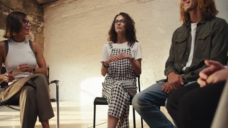 zoom in: a brunette girl with curly hair wearing glasses in a checkered jumpsuit expresses her point of view in a white brick hall