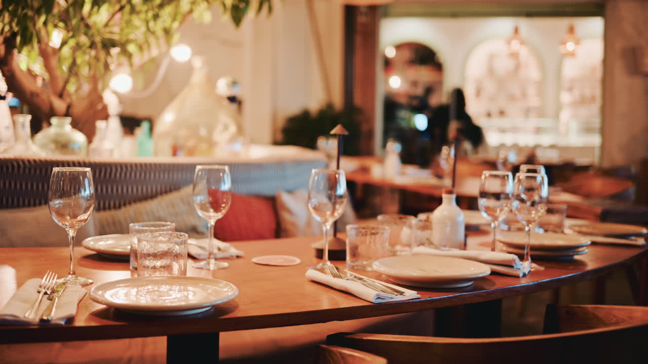 Cinematic shot of a cozy restaurant interior with warm lighting, wooden furniture, wine glasses and a refined table setup
