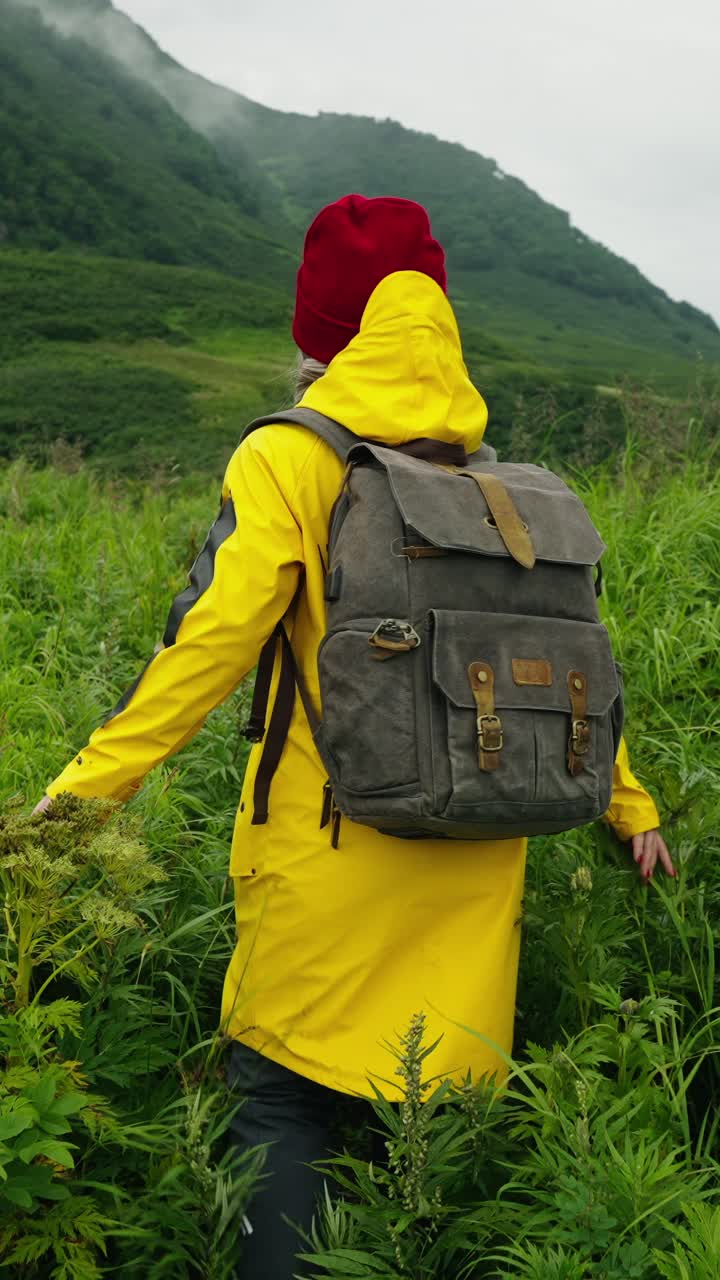 Donna in impermeabile giallo che fa trekking in un prato di montagna verde