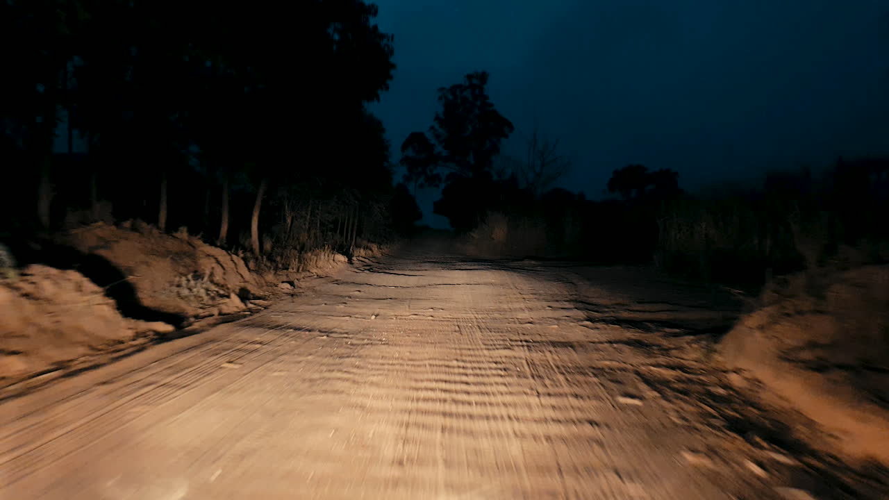 Driving along dirt road lit up by car headlights at night