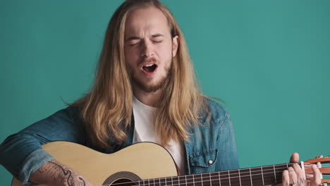 un joven caucásico tocando la guitarra y cantando ante la cámara.