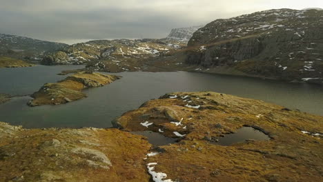 hombre corriendo en la cima de una montaña en noruega con lagos y nieve, movimiento de drones hacia adelante