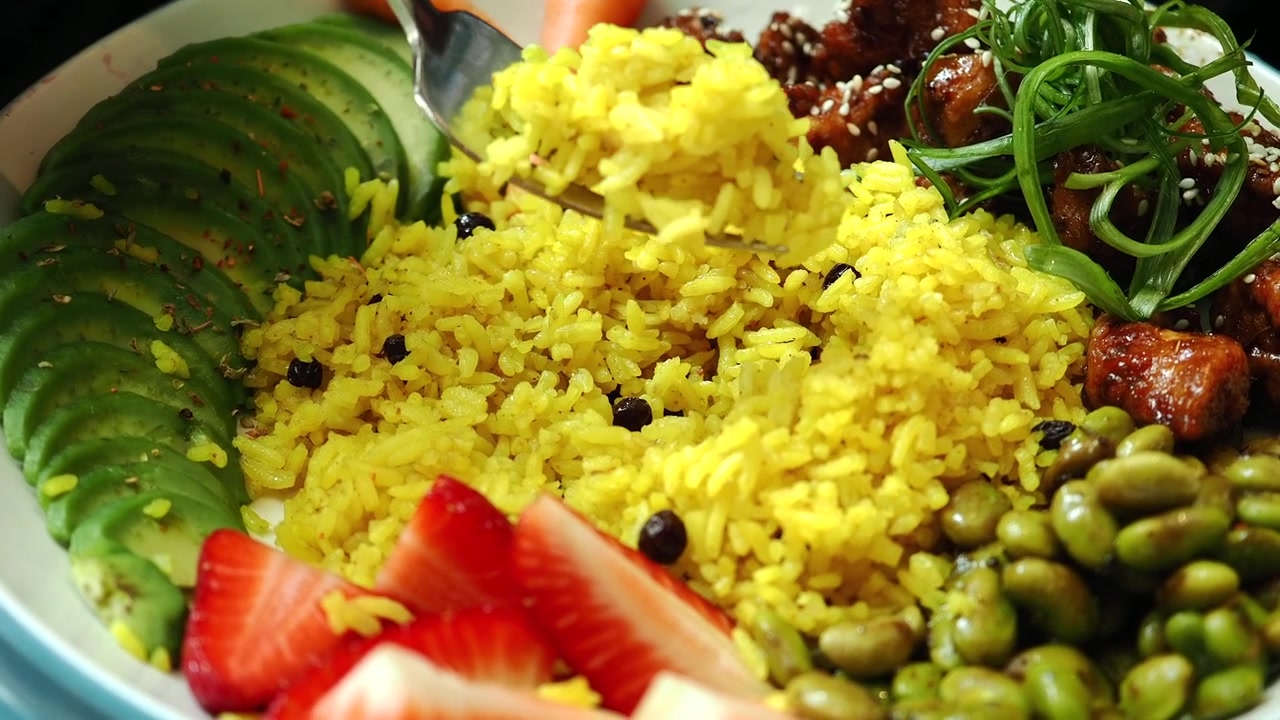Primo piano di una forchetta che raccoglie riso giallo da una Buddha Bowl