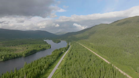 drone flyover scenic norwegian landscape, highway by the namsen river surrounded by lush spuce forest