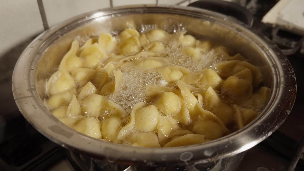 Cappelletti che bollono in acqua dentro una pentola di metallo, ripresi durante la cottura su un fornello in cucina