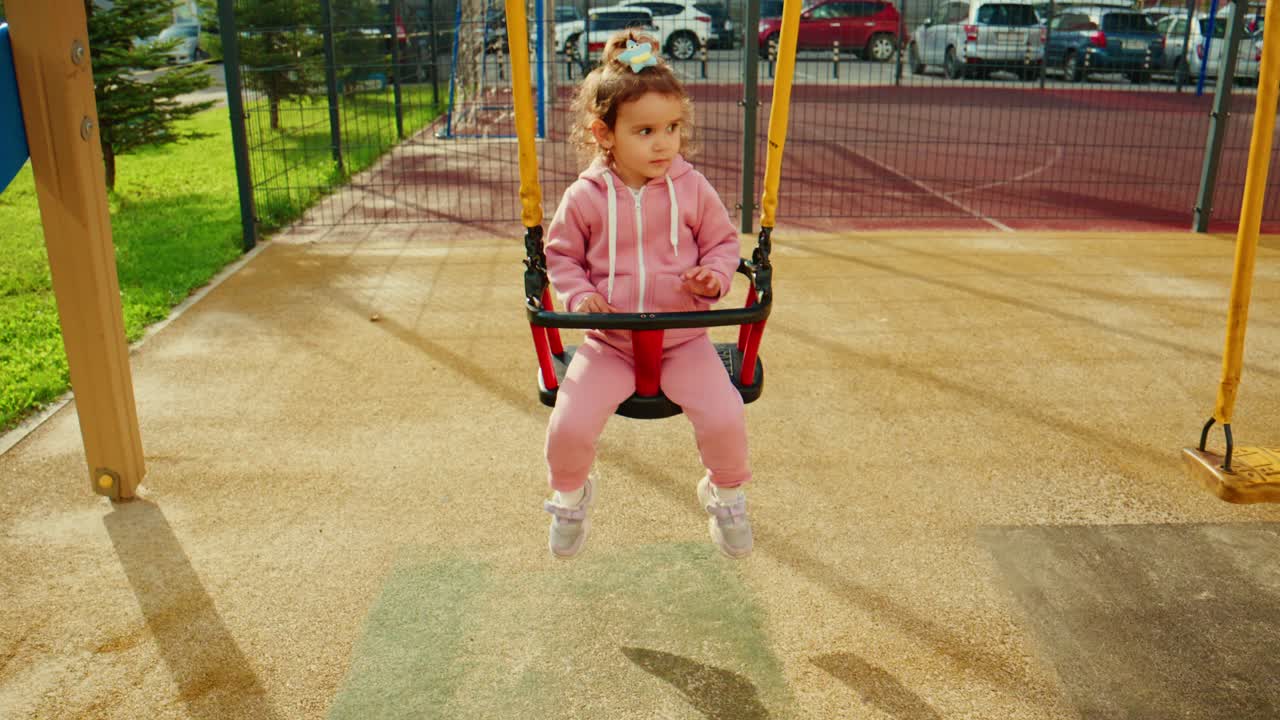 Un bambino piccolo si diverte sull'altalena al parco giochi, immortalando momenti di gioia e allegria in un ambiente esterno vivace, pieno di sole e amicizia