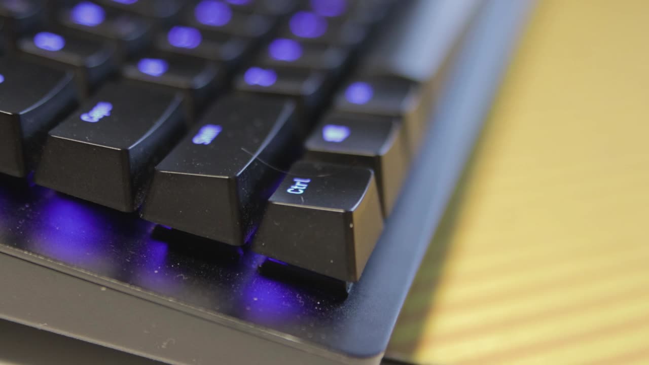 mano presionando una sola tecla en un teclado negro ligeramente polvoriento con teclas retroiluminadas azules