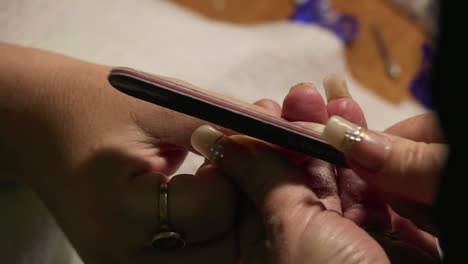 Close-up of a nail technician shaping artificial nails using a nail file.