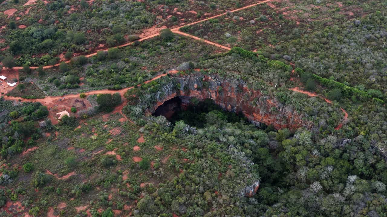 브라질 북동부 바히아에 있는 차파다 디아만티나 국립공원 아래에 자급식 열대우림이 있는 다채로운 바위의 대형 라파 도세 동굴 입구의 넓은 샷을 회전하는 공중 드론