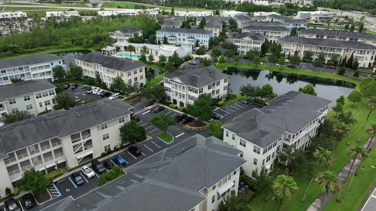 Aerial flyover luxury apartment townhouses in Florida, USA. Private community swimming pool and pond in noble neighborhood of Celebration Town, United States. Wide shot.