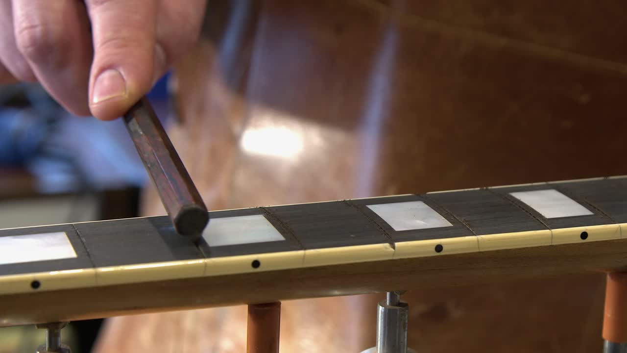 Primo piano: tecnico di chitarre allarga gli slot della tastiera in ebano su chitarra elettrica
