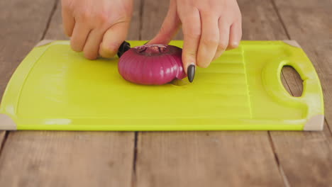 women cutting red onion in half on chopping board