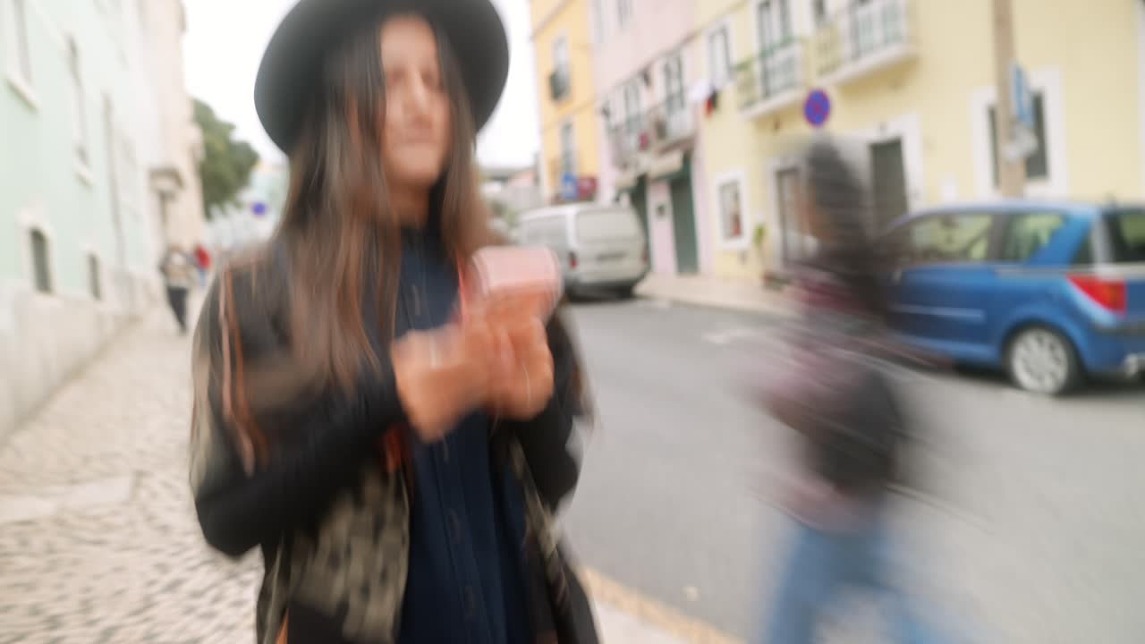 Giovane donna con cappello che cammina e usa lo smartphone per strada