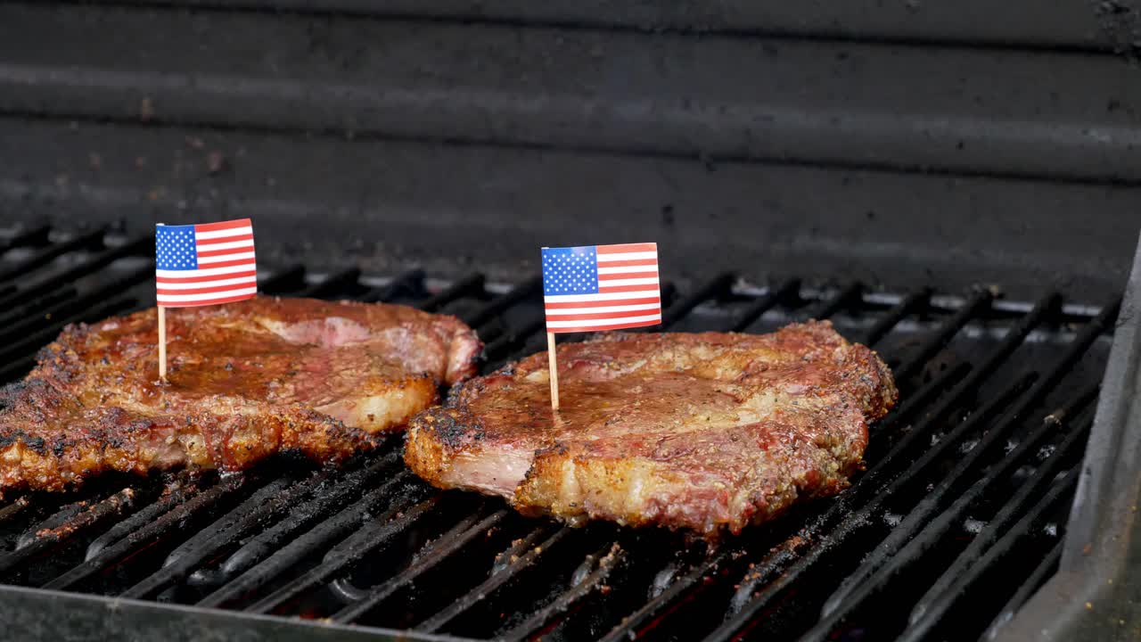 dos bistecs de rib-eye jugosos sentados en la parrilla y cocinados con dos diminutas banderas americanas metidas en ellos