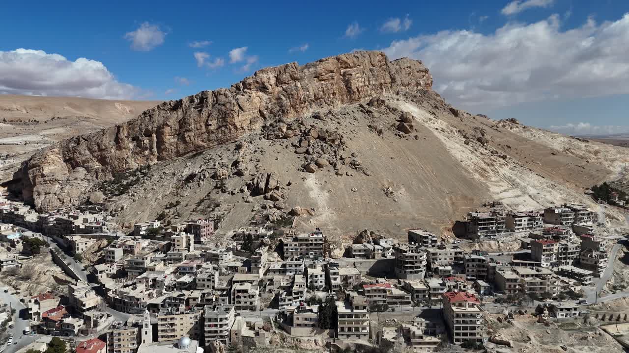 Panoramic drone vista of the historic town of Ma'loula, Syria, highlighting its dramatic geographical setting within the rocky peaks of the Qalamoun range