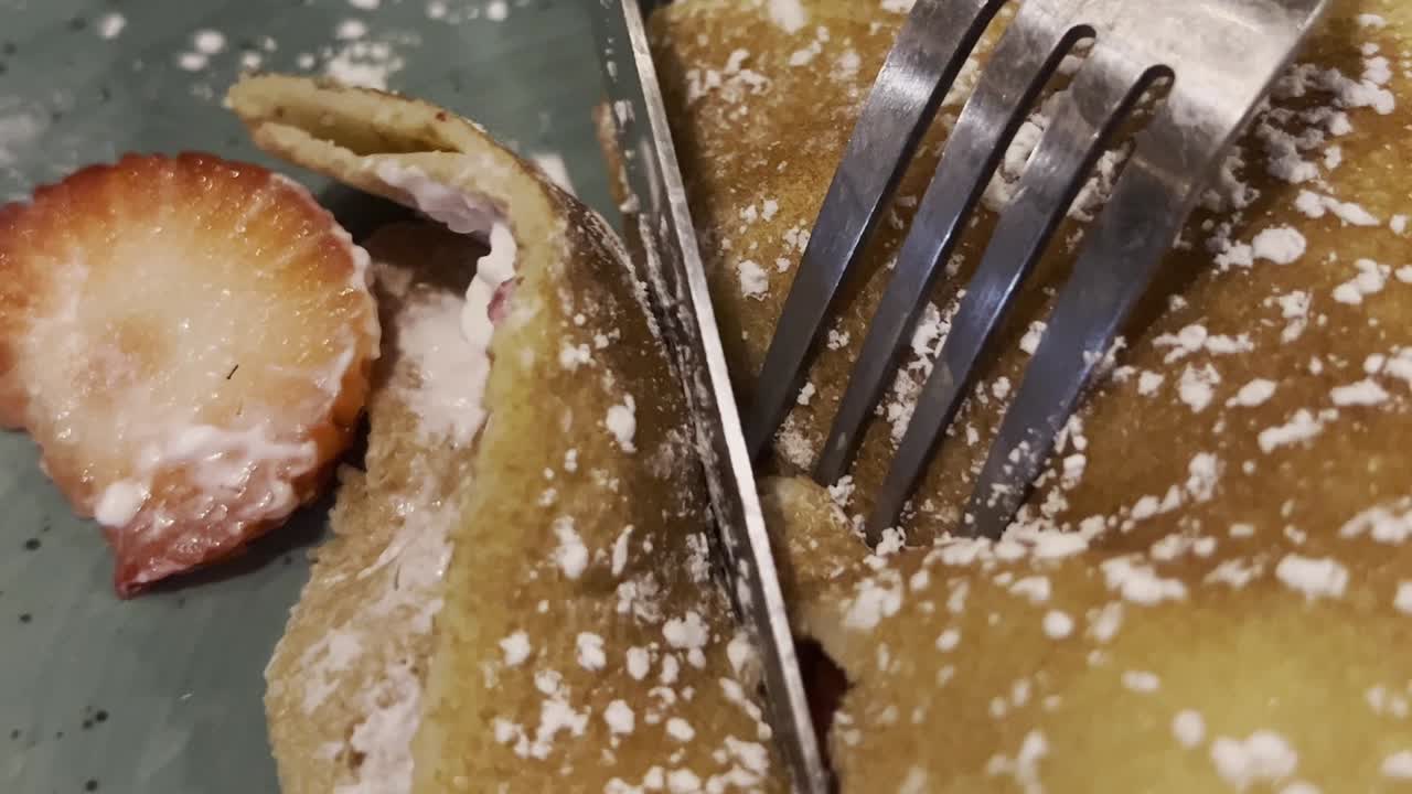 primer plano de un tenedor cortando un strudel lleno de relleno dulce, salpicado de azúcar en polvo