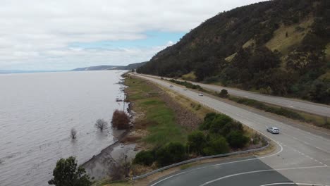 Aerial-view-of-a-car-merging-into-traffic-from-a-rest-area-near-a-muddy-lake