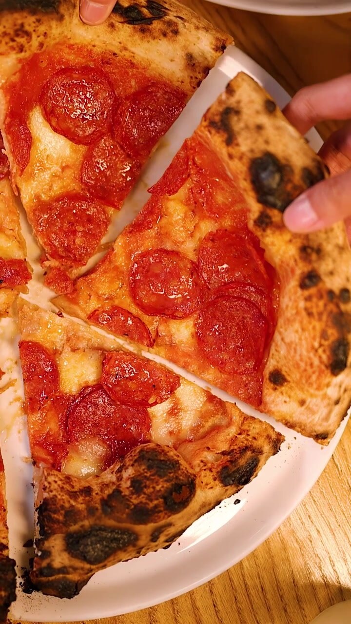 Vista dall'alto di persone che condividono una pizza napoletana al lievito madre con salame piccante durante una cena sociale.