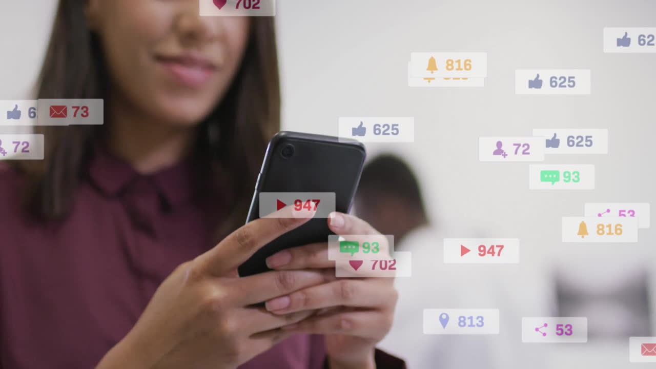 animación de iconos y números sobre mujer de negocios biracial usando teléfono inteligente en la oficina
