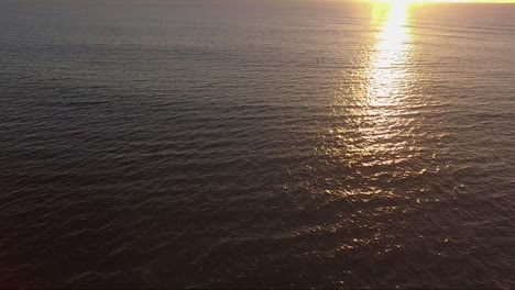 sunrise drone shot over water with paddle boarders passing through golden light rays