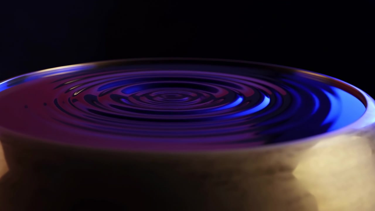 Close-up motion showing concentric rings spreading across glossy circular surface inside textured metal rim, with colored directional lighting, dark reflective background, and sleek metallic finish