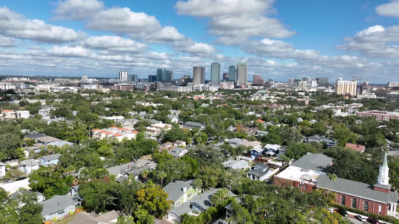 Bairro nobre de Hyde Park em Tampa, Flórida. Ruas residenciais arborizadas e casas históricas cercam uma igreja proeminente, com o horizonte do centro de Tampa ao fundo. Ampla foto aérea para melhorar a qualidade das imagens