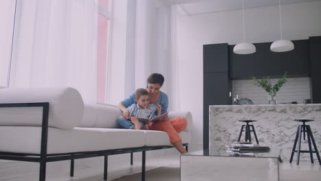 Mother-Sitting-With-Son-Reading-Story-Indoors