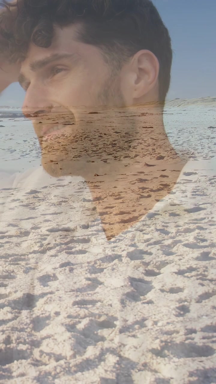 Video verticale: Uomo che si gira verso la spiaggia mentre la brezza gli scompiglia i capelli, con un effetto sabbia sul viso per il marketing.