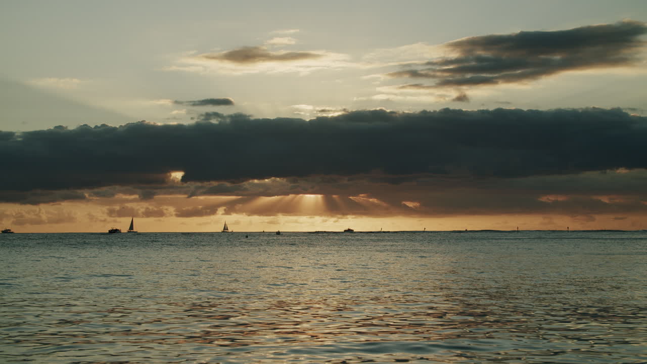 Golden Sunset over the Ocean with Distant Boats and Sun Rays Breaking Through Clouds