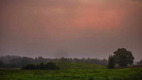 gray, foggy morning turns golden as the sunrise illuminates the sky above lush, green countryside - time lapse