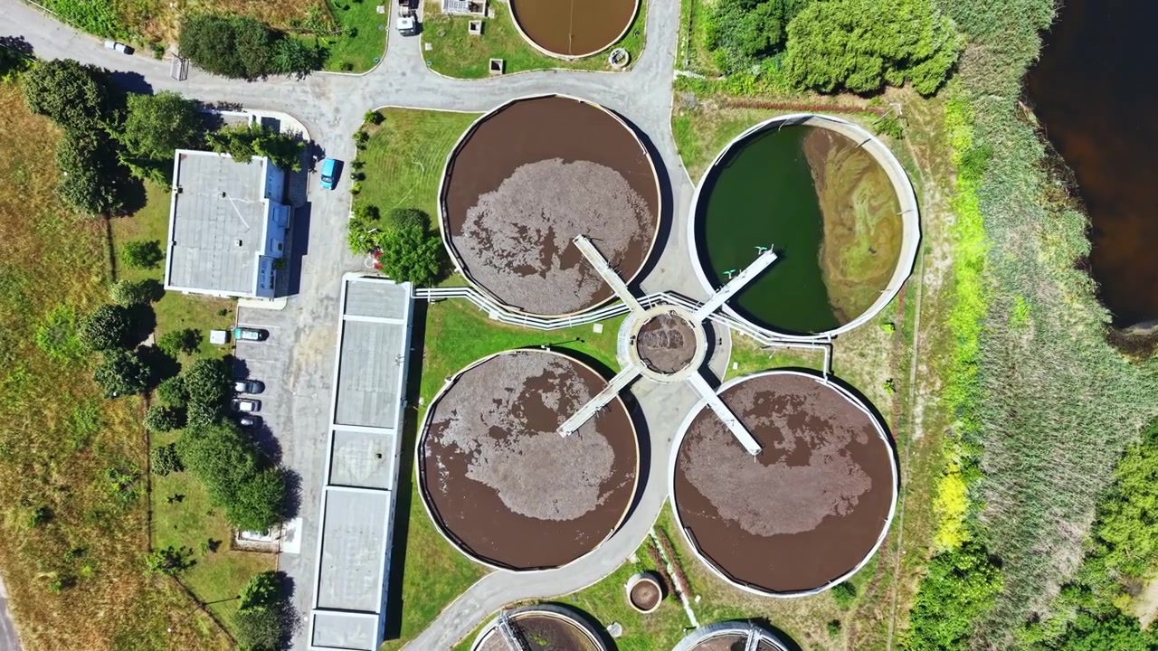 Planta de tratamiento de agua con tanques circulares vista desde arriba con la luz de la tarde cerca de un río y una zona verde.