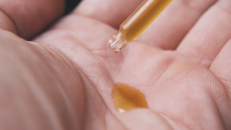 person drops liquid from pipette on palm in black background