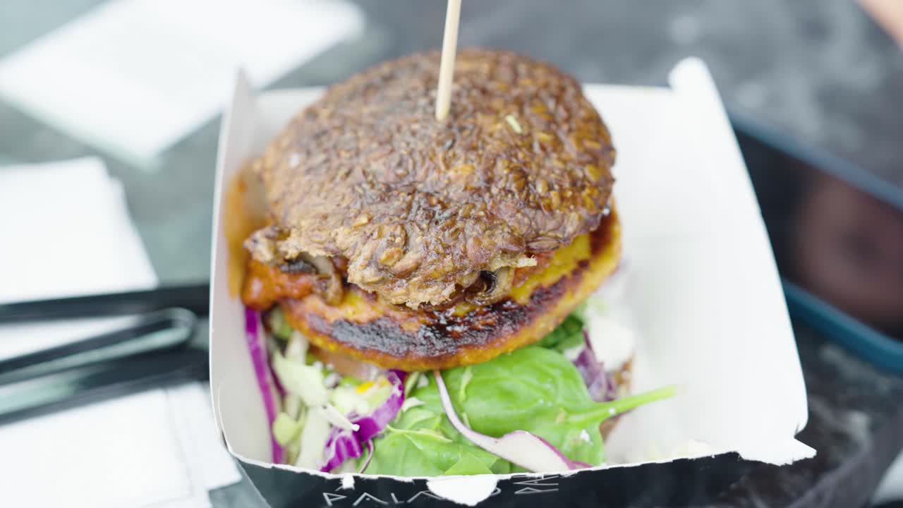 Close up of vegan burger in cardboard box, girl pick salad leaf with fork