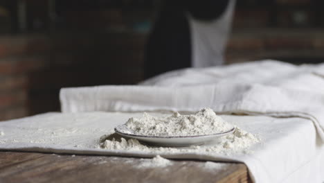 spilled flour and baking cloth on a wooden table with woman baker in the background