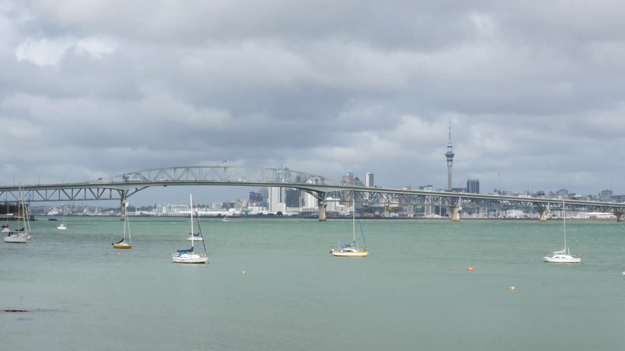 Auckland's Iconic Harbour Bridge with Yachts in the Foreground and Cityscape in the Background on a Cloudy Day, New Zealand