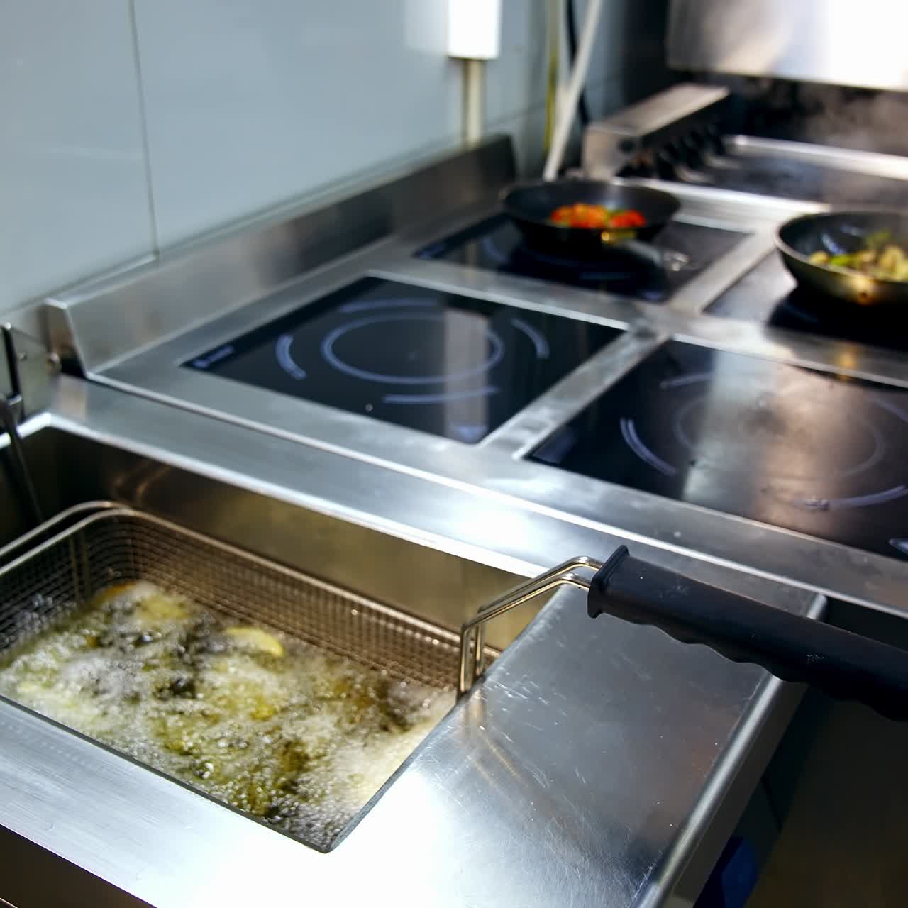 Preparando refeições na cozinha do restaurante. Batatas fritas numa fritadeira, com frigideiras no fogão ao fundo. Batatas crocantes numa fritadeira.