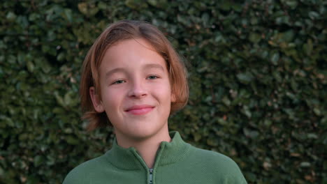 boy laughing by a leafy fence