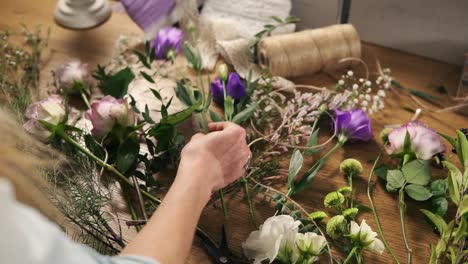joven florista rubia preparando flores para un ramo. manos de dueña de un tiro de flor trabajando en su tiro de flor haciendo un ramo