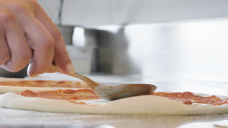 primer plano de un chef irreconocible esparciendo salsa de tomate con una cuchara en la masa cruda de pizza en el restaurante 2