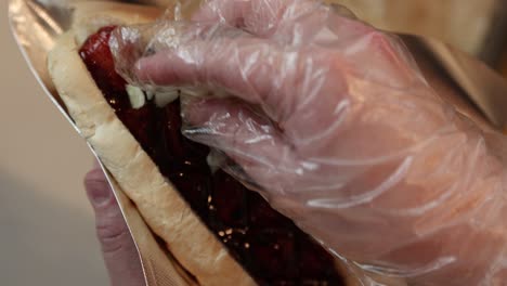 fotografía de cerca de la mano rociando cebollas picadas en un perrito caliente