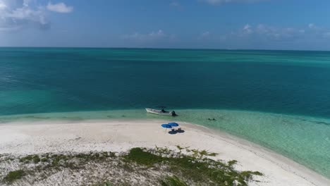 Luftaufnahme-Drehen-Sie-Sich-Um-Den-Wunderschönen-Karibischen-Strand-Mit-Boot-Und-Ein-Paar-Strandkörben-Für-Einen-Romantischen-Kurzurlaub-Auf-Einer-Tropischen-Insel