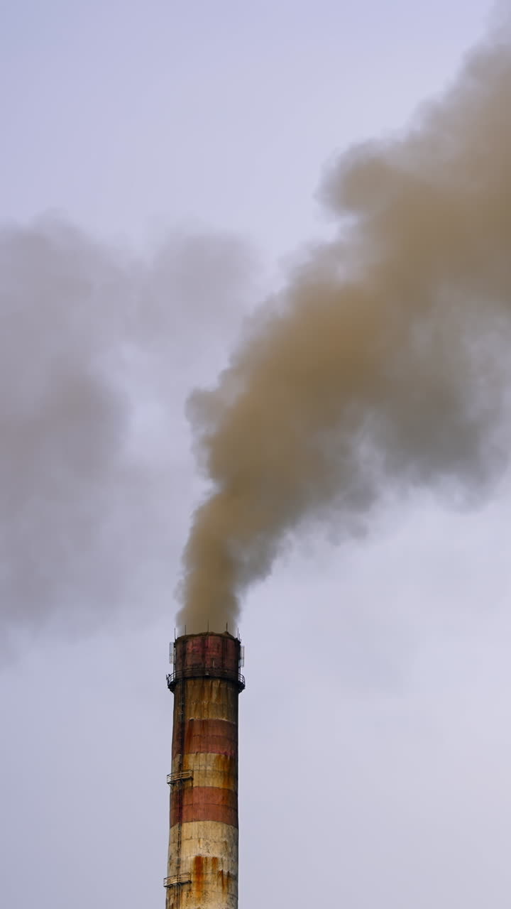 Dangerous emissions on the sky background. Dark toxic smoke clouds coming out of factory chimney. Air pollution and global warming. Vertical video