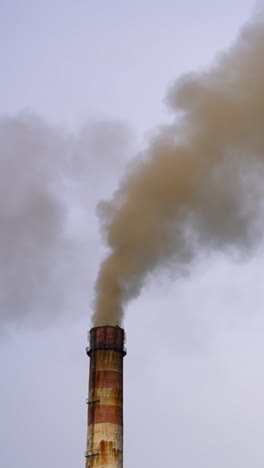 dangerous emissions on the sky background. dark toxic smoke clouds coming out of factory chimney. air pollution and global warming. vertical video