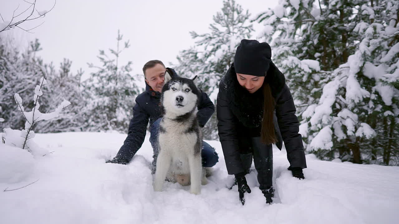 hermosa familia, un hombre y una niña en el bosque invernal con un perro. juega con el perro husky siberiano.